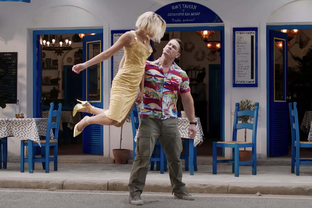 John Cena lifts up Dua Lipa with one arm in front of a restaurant in Argylle (2024).