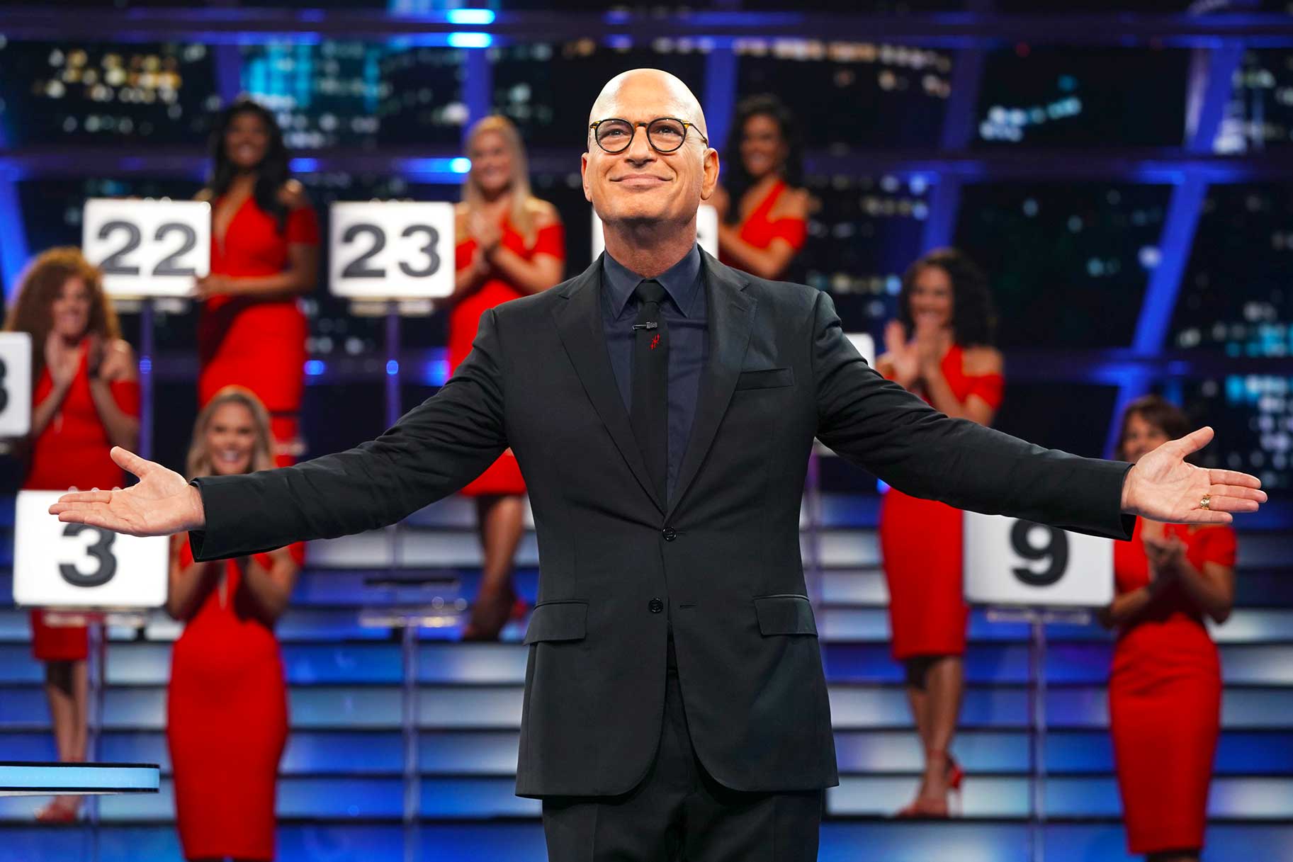 Howie Mandel posing with his arms out with the Briefcase Models wearing red dresses in the background.