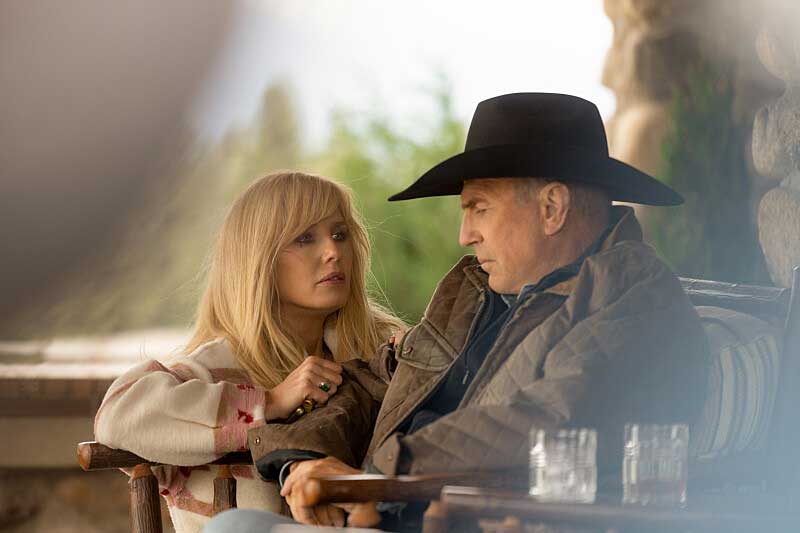 Beth Dutton crouching next to John Dutton who is seated in a chair.