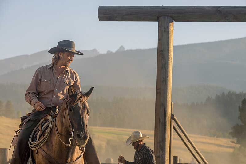 Kayce Dutton riding a horse outdoors next to wooden beams.