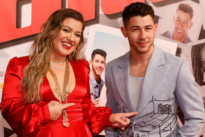 Kelly Clarkson posing and pointing at Nick Jonas on a red carpet