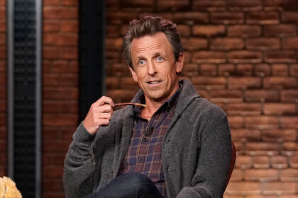 Seth Meyers sitting in a chair, smoking a pipe