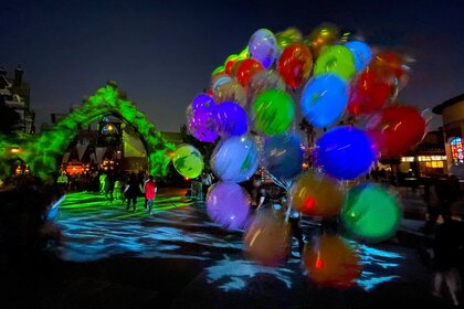 Guests walking down a dark pathway that's lit up green with balloons in the view.