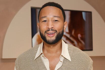 John Legend smiling wearing a beige sweater at an event