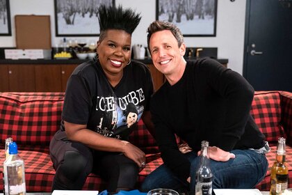 Leslie Jones and Seth Meyers smiling and posing together on a plaid couch.