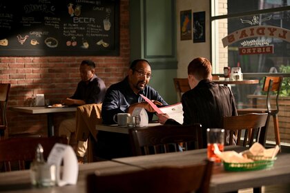 Alec Mercer sitting across another character in a coffee shop.