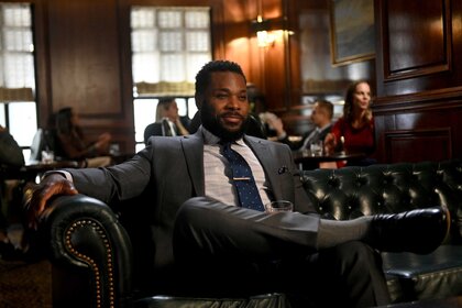 Dustin Atwood wears a suit while sitting on a leather couch with his legs crossed.