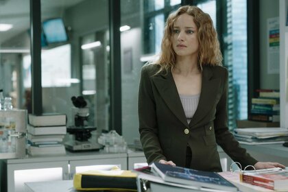 Dr. Magalie Leblanc, wearing an olive green blazer, standing over a desk with books.