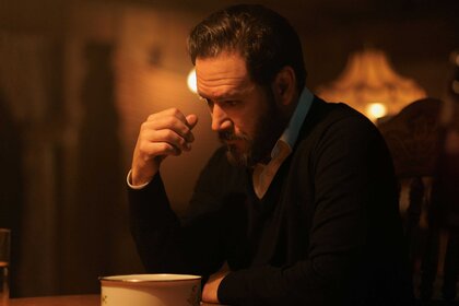 A close-up of Sir sitting at a table with his head looking down at a bowl.