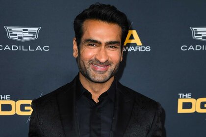 Kumail Nanjiani wearing a black blazer and smiling on the red carpet.