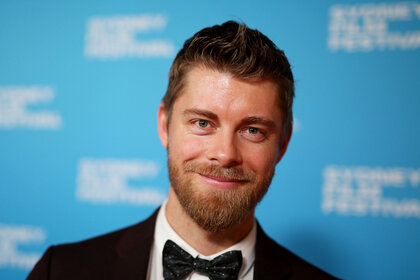 Luke Mitchell standing and smiling in front of a step and repeat.