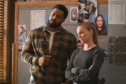 Kevin Atwater and Hailey Upton stand in front of a bulletin board in the squad room on Chicago PD 1104