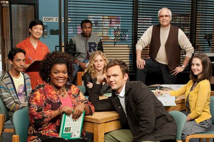 The cast of Community sitting at a table in a library for a promo shoot