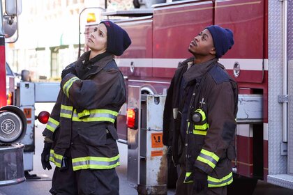 Stella Kidd and Darren Ritter stand near a fire truck in firefighter gear in Chicago Fire Episode 1202.