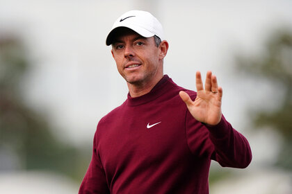 Rory McIlroy waves on the golf course in a white hat and red shirt