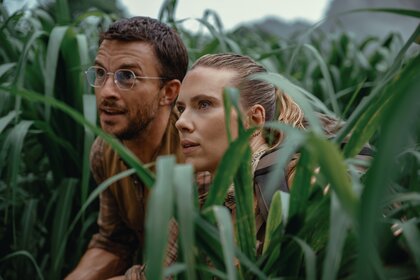 Dr. Henry Loomis (Jonathan Bailey) and Zora Bennett (Scarlett Johansson) hide in tall grass in Jurassic World Rebirth (2025).