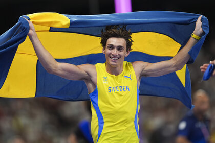 Armand Duplantis holding the Swedish flag and smiling at the Paris 2024 Olympics.