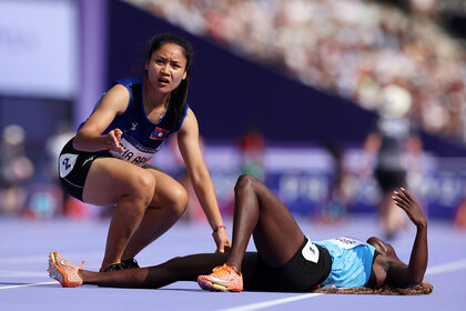 Lucia Moris of Team South Sudan lies injured on the ground as Silina Pha Aphay of Team Lao checks her condition during the Women's 100m Preliminary Round on day seven of the Olympic Games Paris 2024