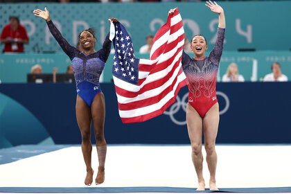 Simone Biles and Suni Lee hold up the american flag after winning medals at the 2024 olympics