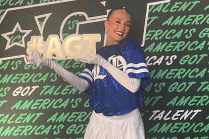 Emily Gold poses with a sign that says #AGT on it at America's Got Talent