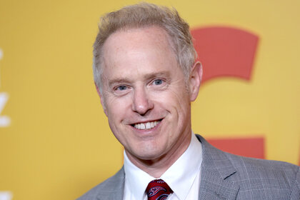 Raphael Sbarge smiles on the red carpet in a grey suit