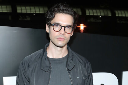 Steven Strait wears a grey jacket and glasses at a party