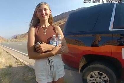 Gabby Petito stands outside of a SUV holding water bottles while talking to the police