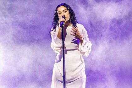 Charli XCX performs in a white dress onstage.