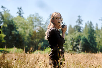 Rebecca Henderson walks in a field with a walkie talkie on The Hunting Party Season 1 Episode 3.