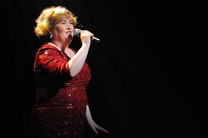 Susan Boyle performs onstage in a red dress.