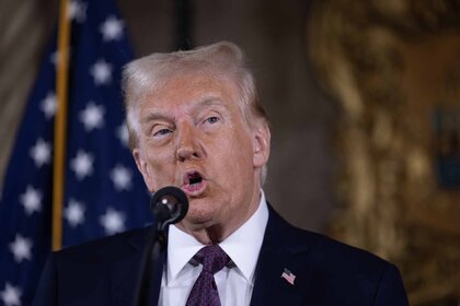 Donald Trump speaks into a mic white an American flag hangs in the background.