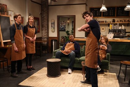 Five people with tan aprons on standing in a coffee shop set on SNL.