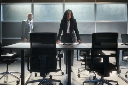 Jacob Hassani (Patrick Sabongui) watches Elizabeth Mallory (Zabryna Guevara) lean on a desk in The Hunting Party Episode 102.