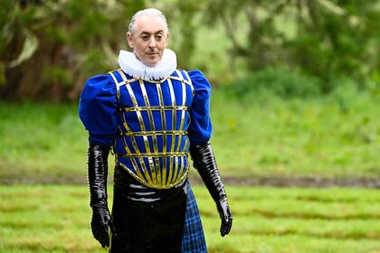 Alan Cumming outside wearing a blue victorian outfit on The Traitors Season 3, Episode 10.