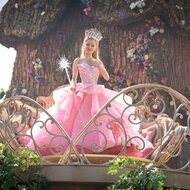 Glinda holds her wand up in a puffy pink dress in Wicked