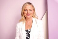 Amy Poehler, wearing a white blazer, smiles at the camera at an event.