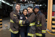 Matthew Casey, Gianna Mackey, Stella Kidd, and Darren Ritter hugging and posing for a photo in their firefighter jackets.