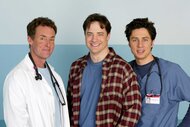 Dr. Perry Cox, Ben Sullivan, and Dr. John Dorian standing next to each other and smiling on the set of Scrubs.