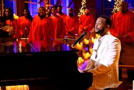 John Legend singing and playing piano while a choir is singing in the background.