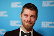 Luke Mitchell standing and smiling in front of a step and repeat.