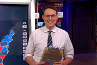 Steve Kornacki smiles and holds a clip board on The Tonight Show Starring Jimmy Fallon