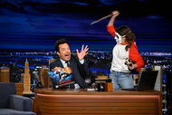 Jimmy Fallon at his desk getting scared by a person holding a knife wearing a mask