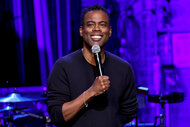 Chris Rock smiles on stage holding a microphone