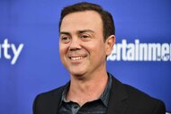 Joe Lo Truglio smiles in front of a blue backdrop.