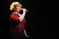 Susan Boyle performs onstage in a red dress.