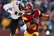 Jayden Daniels of the Washington Commanders holds the ball and avoids a Philadelphia Eagles player during a game.