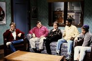 The men of Saturday Night Live sit on a couch together during a sketch.