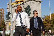 Jalen Shaw on a walkie talkie standing next to Vincent Riley outside on Law & Order Season 24 Episode 9.