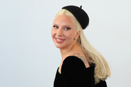 Lady Gaga smiles in a black beret and black dress.