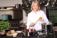 Martha Stewart smiles in her kitchen while holding a wooden spoon.